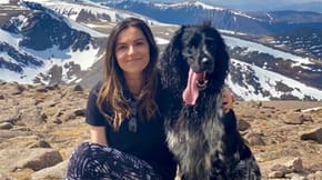 A woman sits on a mountainside with her dog by her side