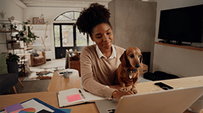 A woman works from home on a laptop, with a Dachshund on her lap