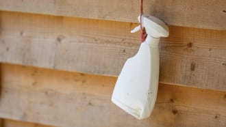 White disinfectant bottle hanging from bailing twine against a wooden stable
