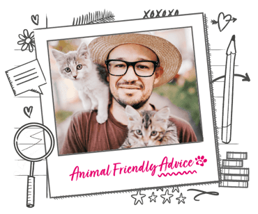 A man in a hat with glasses holds two cats, one of which balances on his shoulder