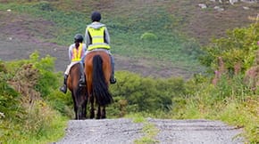2 horses, both with riders wearing hi vis jackets