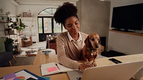 A woman works from home on a laptop, with a Dachshund on her lap