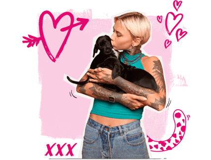 A lady holding two small black puppies and giving one of them a kiss