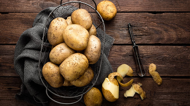 Potatoes on a chopping board, with a potato peeler.