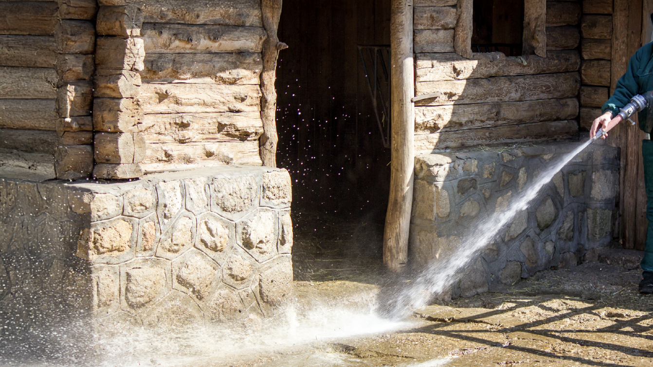 Someone in a green jacket jet-washing the front of a stable
