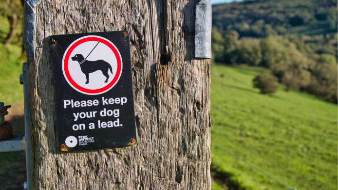 A picture of a sign in the countryside, which says to keep dogs on leads
