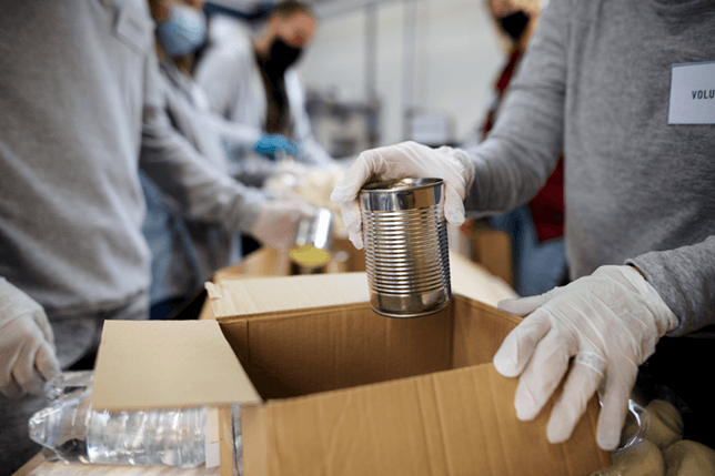 a volunteer adding a tin of dog food into a food parcel